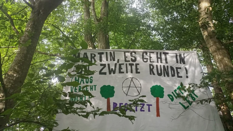 Banner gepannt zwischen Bäumen mit der Aufschrift: Martin, es geht in die zweite Runde. Choas vergeht nicht. Dieti lebt!"